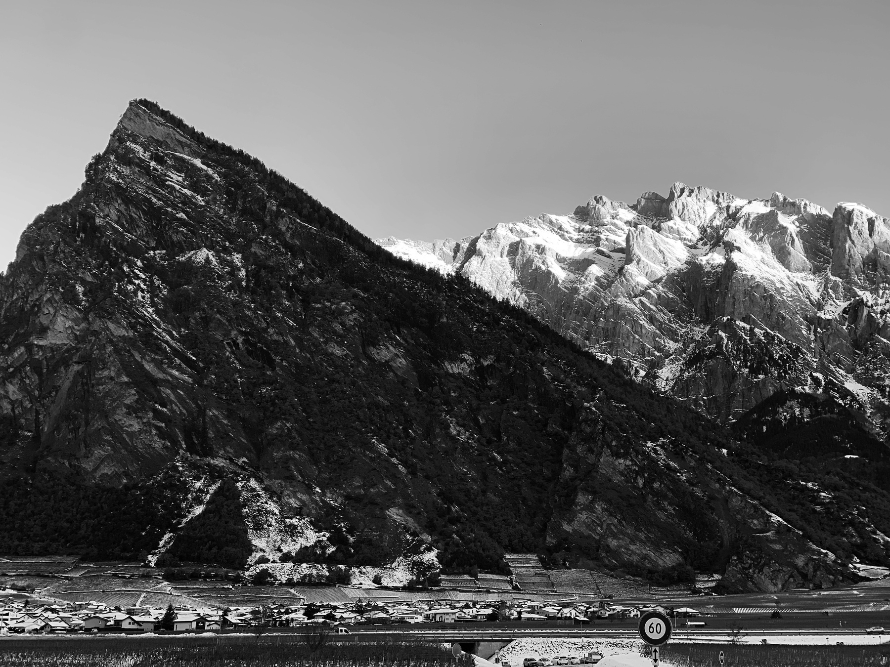 A gauche, une montagne sombre de forme triangulaire devant des sommets enneigés dans la partie droite de l’image. 