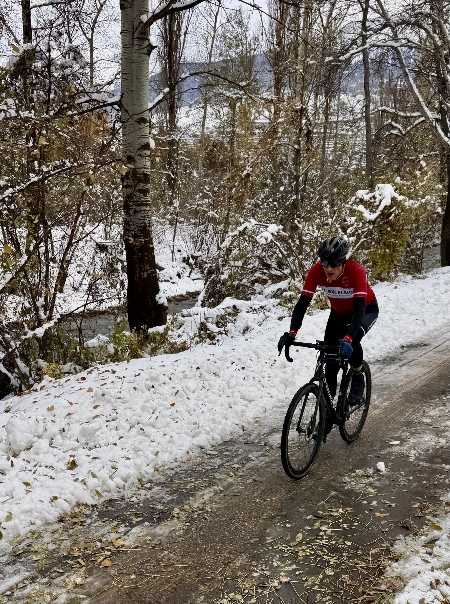 Un cycliste portant un maillot rouge roule sur un chemin enneigé dans une zone forestière.